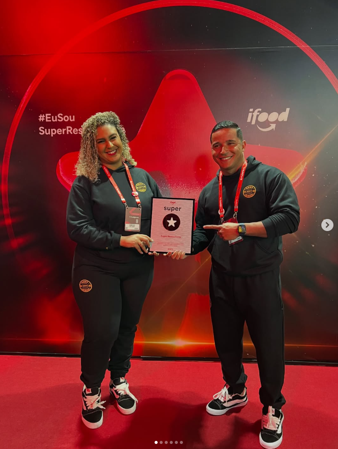 Daniel e Sara com a placa Super Restaurante iFood - Dan's Burger Piracicaba